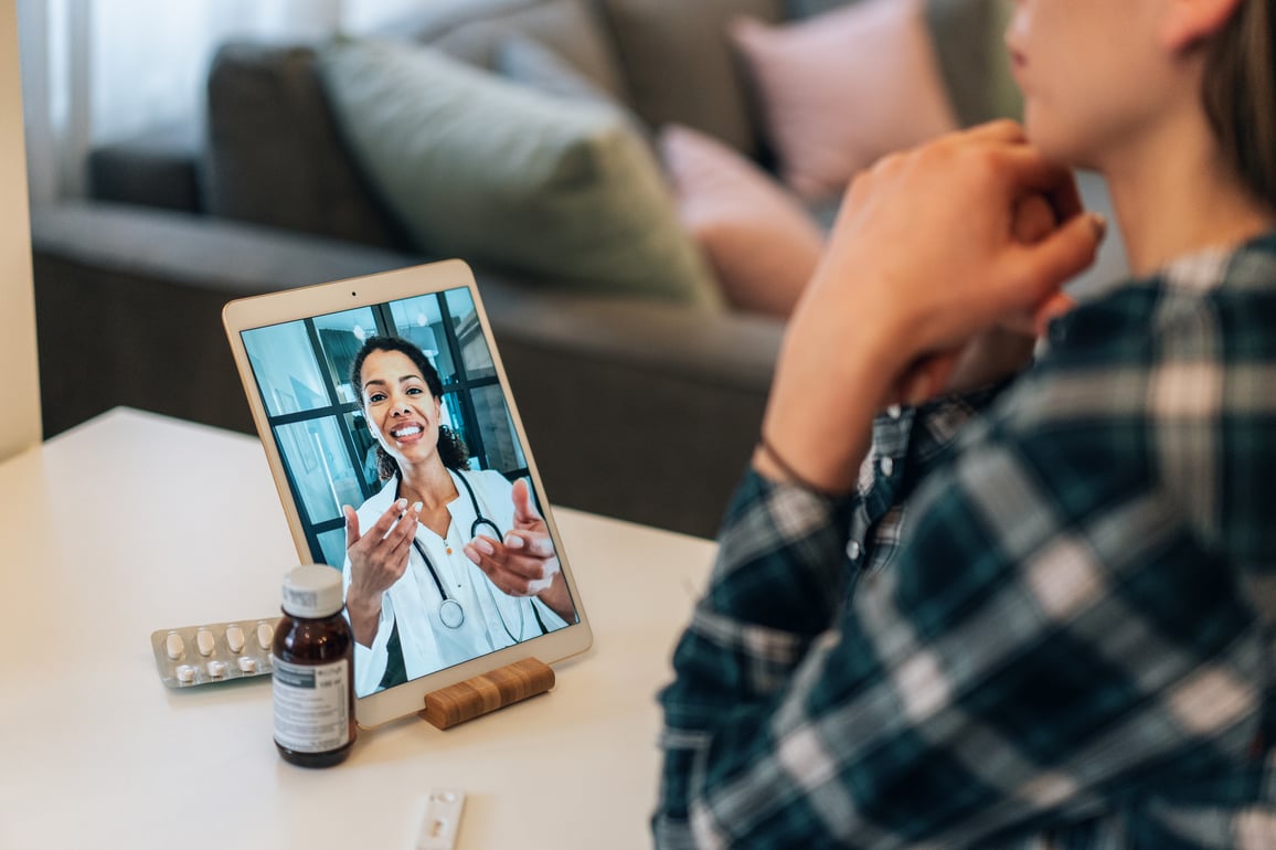 Female doctor in lab coat speaking with patient through tablet video telemedicine call