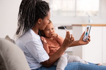 Mom and child smiling at phone taking temperature during virtual primary care visit