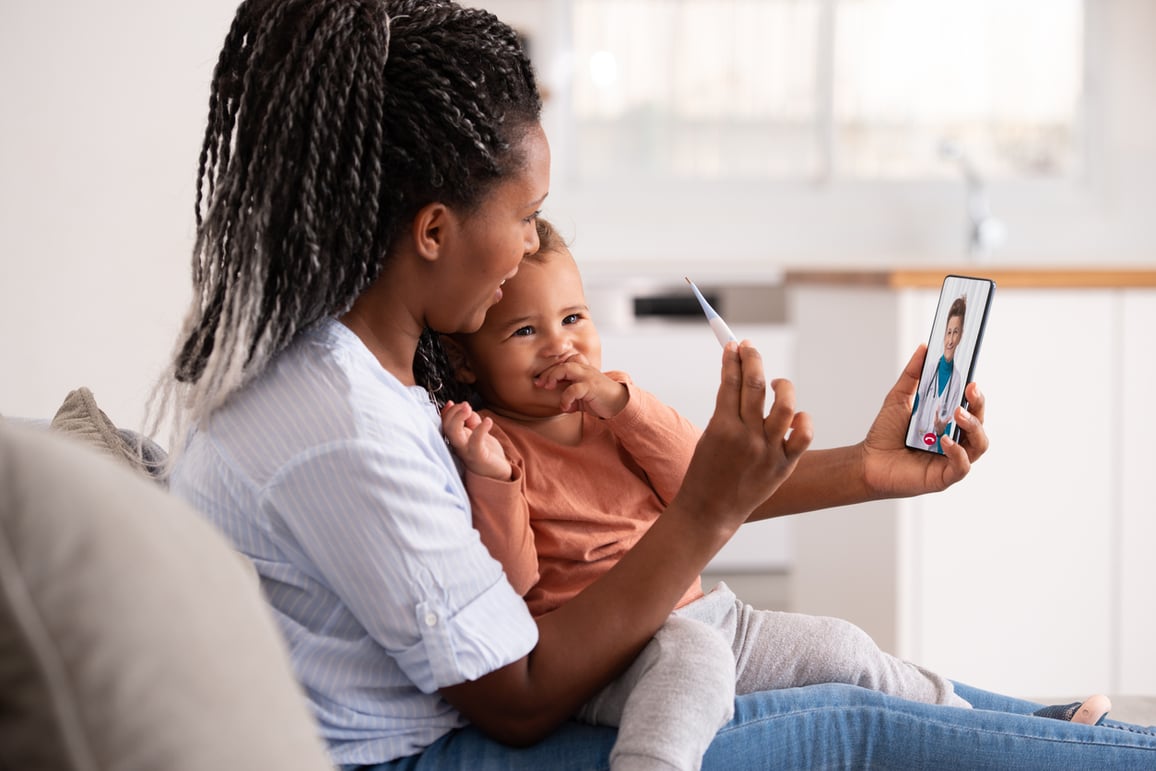 Mom and child smiling at phone taking temperature during virtual primary care visit