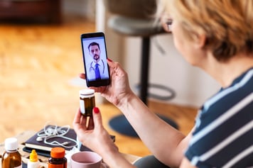 Woman using cell phone on telemedicine video call asking about prescription.