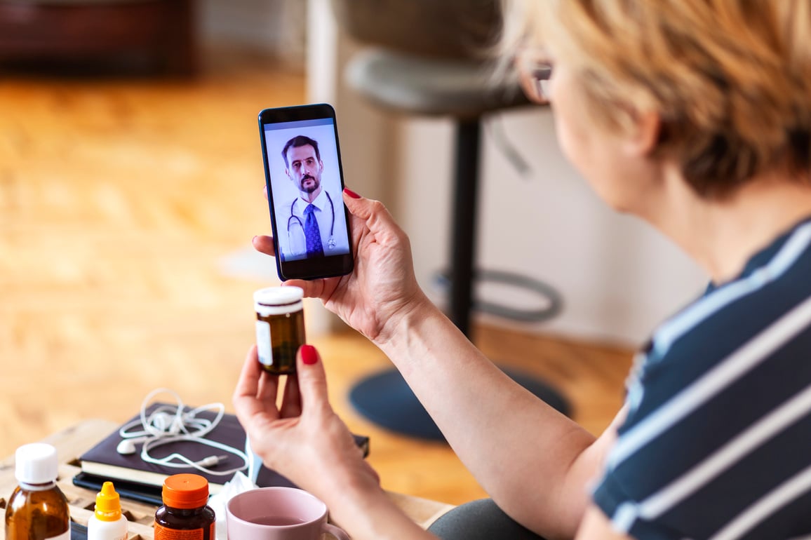 Woman using cell phone on telemedicine video call asking about prescription.