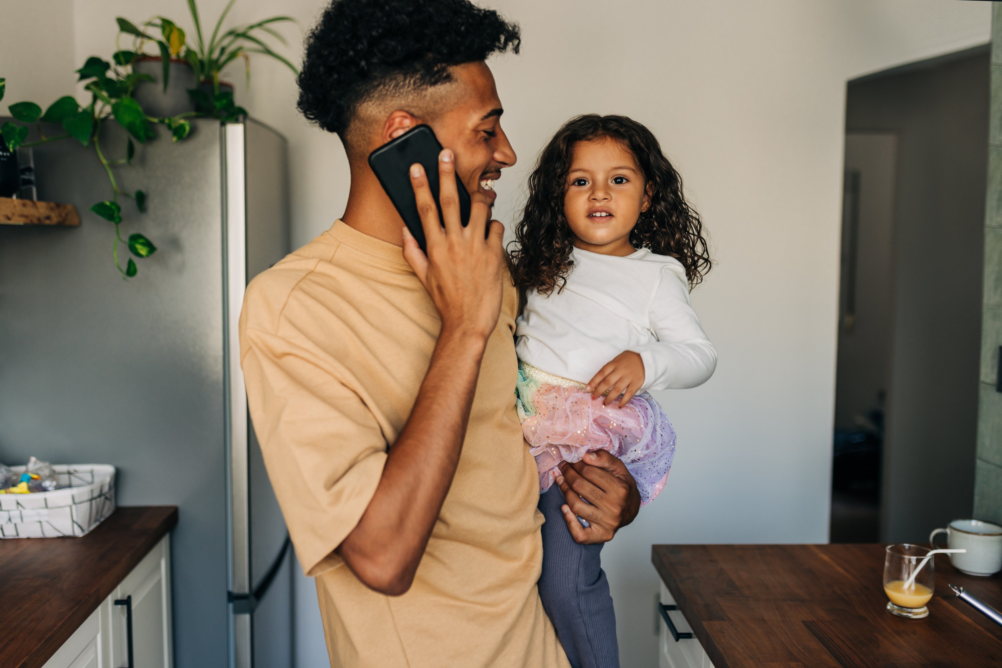 Father holding daughter while on cell phone call with telemedicine doctor in kitchen