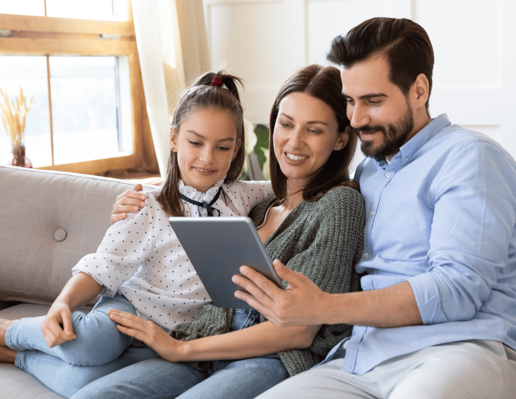 Parents sitting on sofa with daughter using tablet for video telemedicine call with healthcare provider